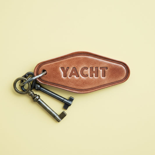 Brown leather keychain with 'YACHT' engraving on a wooden surface