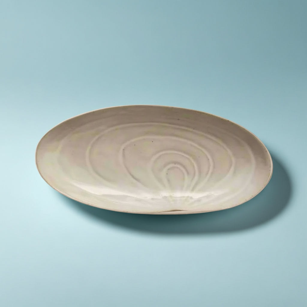 Stoneware plate shaped like a seashell with natural textured detailing displayed on a table.