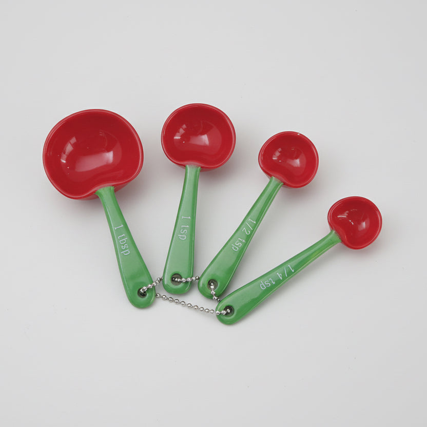 Set of four red measuring spoons with green handles on a white background