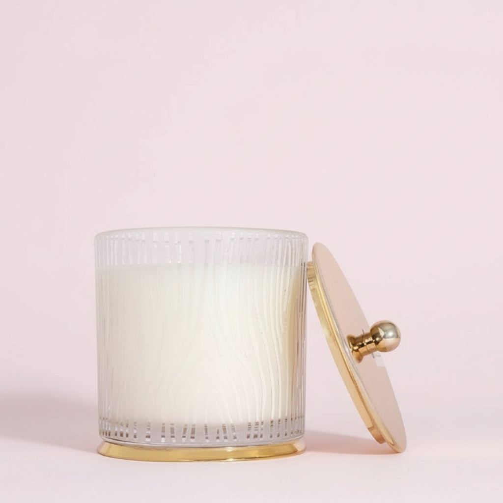 White textured candle with gold base and lid on a white background