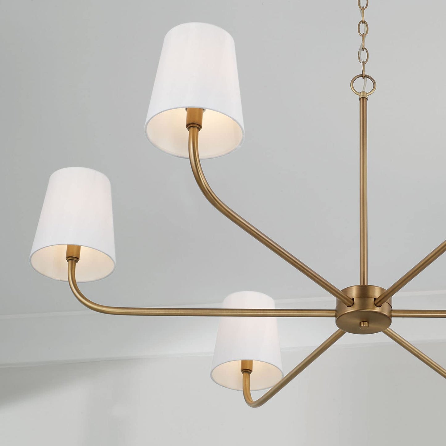 Aged brass chandelier with six white fabric shades, styled with modern curves and timeless warmth.