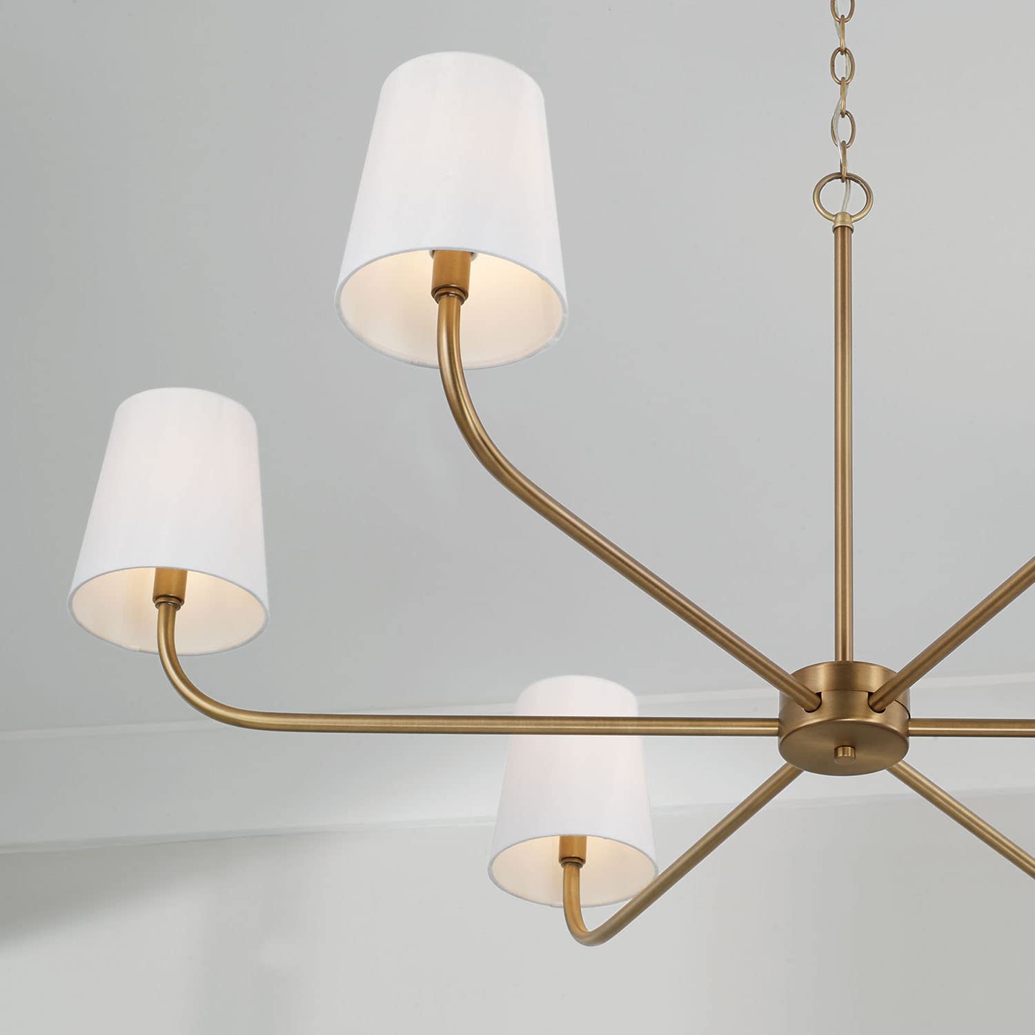 Aged brass chandelier with six white fabric shades, styled with modern curves and timeless warmth.