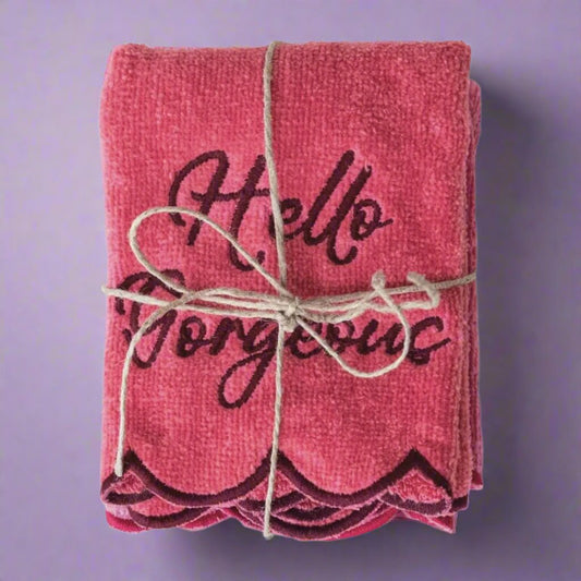 A soft pink towel with the phrase "Hello Gorgeous" embroidered, draped over a bathroom rack for a touch of charm and elegance.