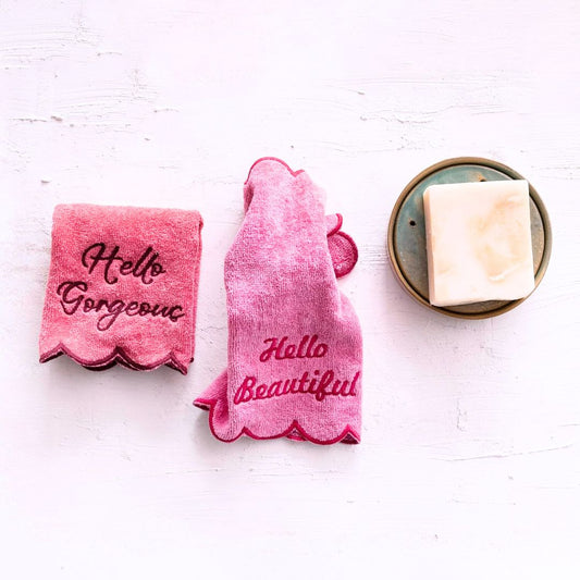 A soft pink towel with the phrase "Hello Gorgeous" embroidered, draped over a bathroom rack for a touch of charm and elegance.