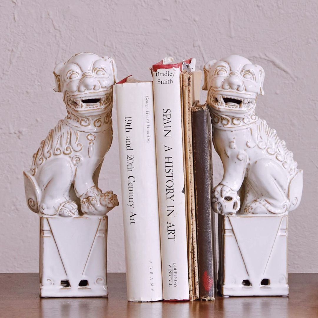 White dog-shaped bookends with intricate details, designed in an elegant, exotic style, placed on a wooden shelf.