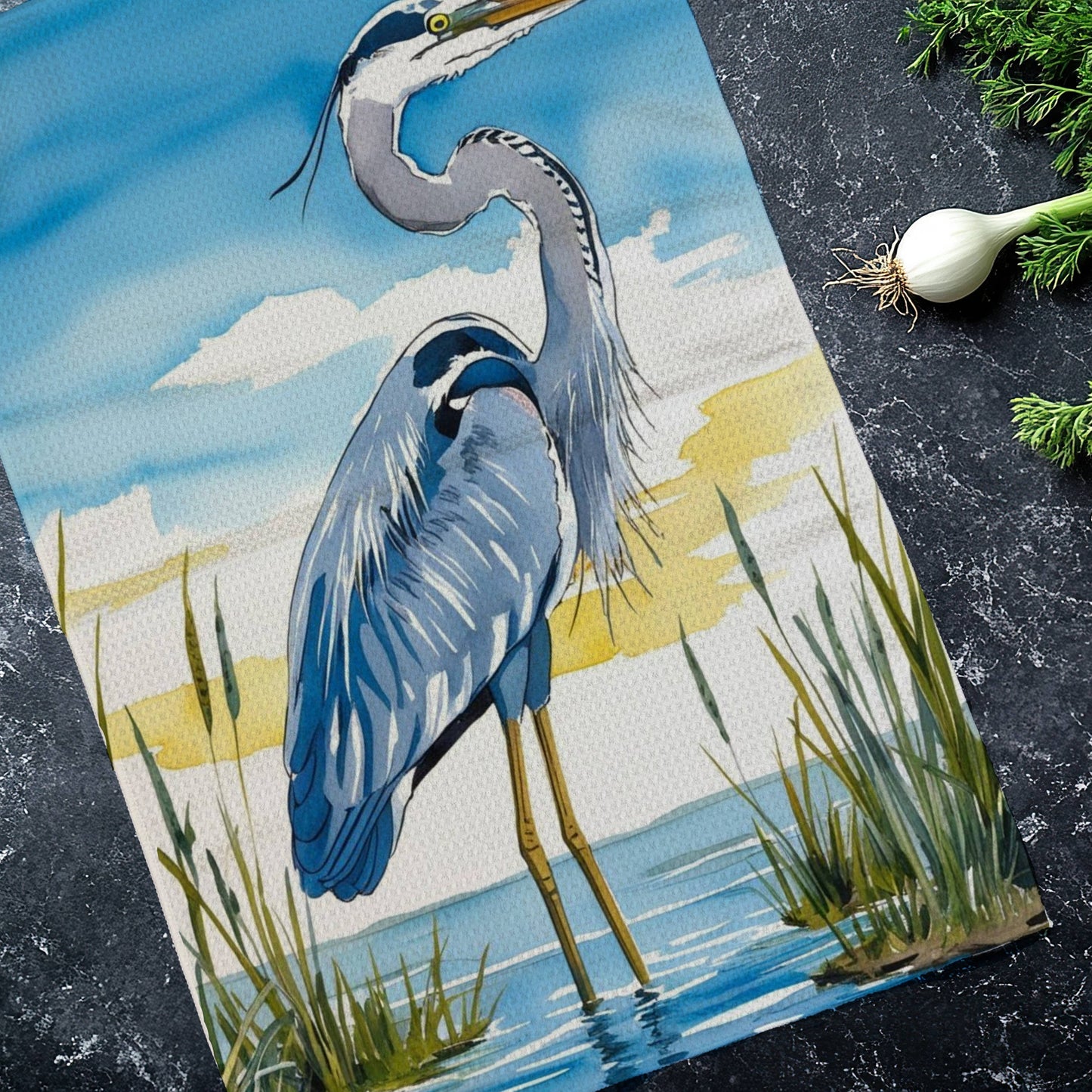 Tea towel with a heron design on a dark surface with green onions.