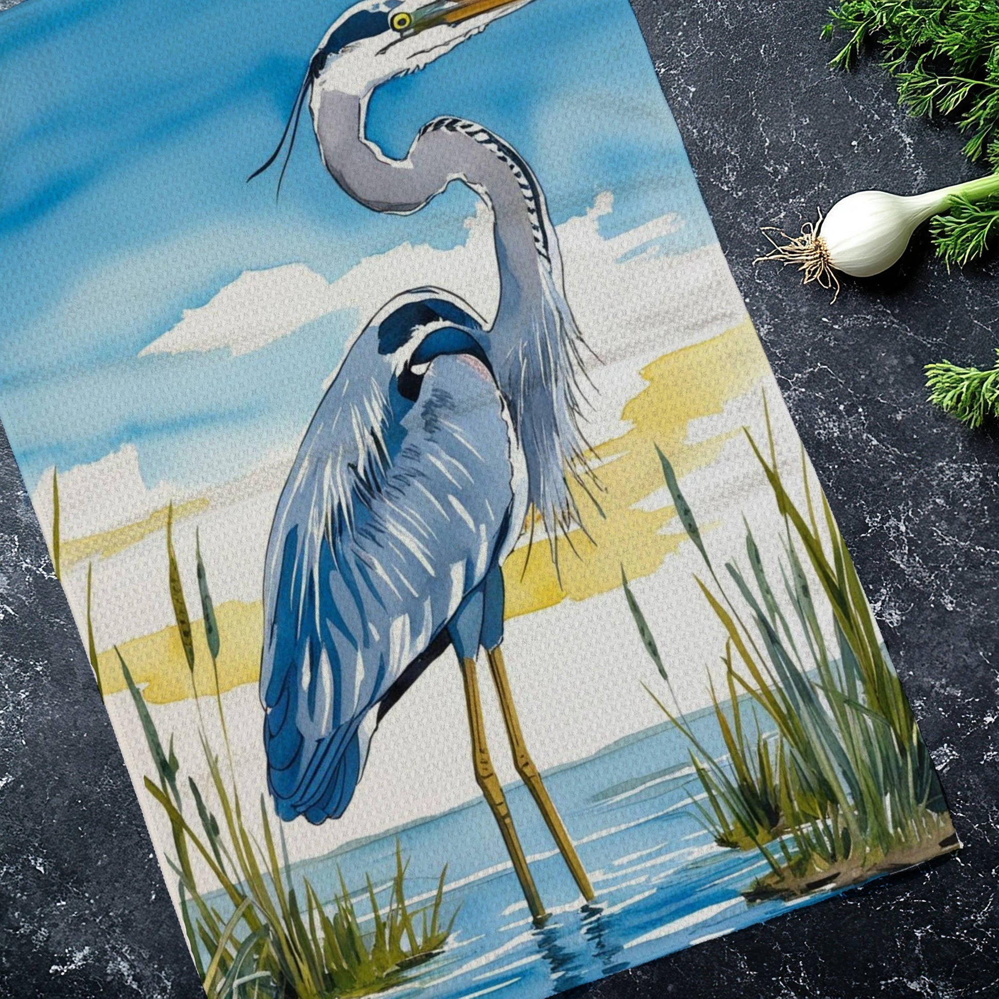 Tea towel with a heron design on a dark surface with green onions.