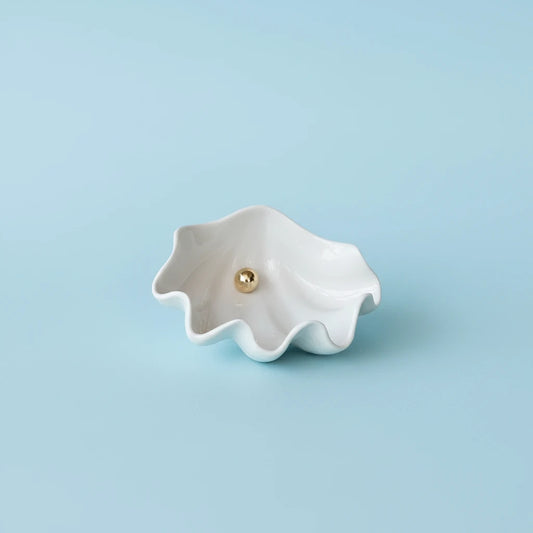 White ceramic shell with a gold pearl on a white surface